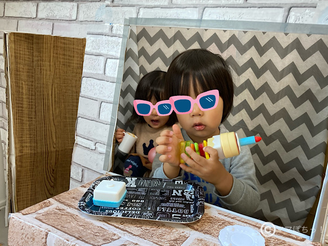 カフェ風ダンボールハウスで遊ぶ2人の子供の写真です。